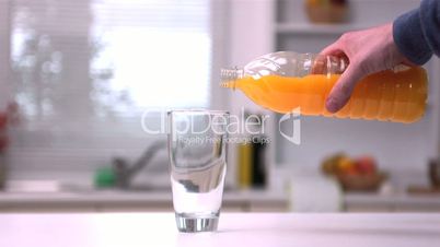 Mans hand pouring orange juice from a bottle into a glass
