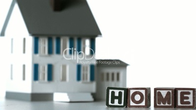 Blocks spelling home sliding along in front of a miniature house