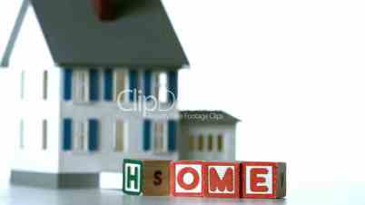 Blocks in row spelling home sliding along in front of a model house
