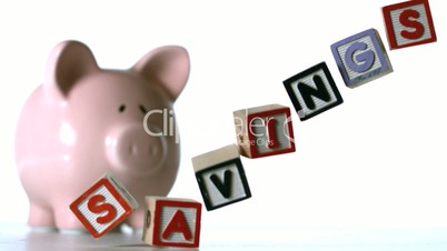 Blocks spelling savings dropping down in front of a pink piggy bank