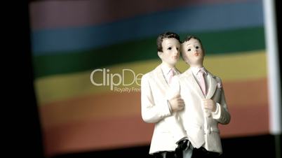 Gay groom cake toppers in front of rainbow flag moving in the wind