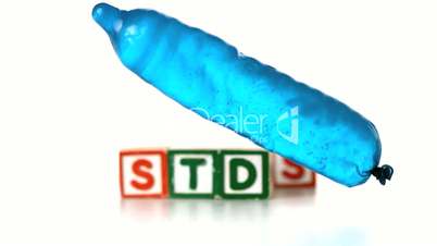 Blue condom filled with water falling and bouncing in front of blocks spelling STDs