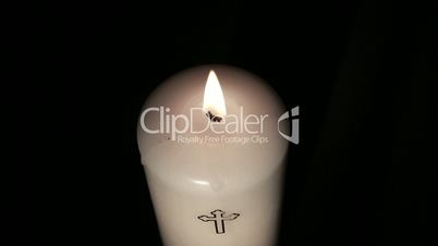 Candle with cross embellishment burning and being blown out