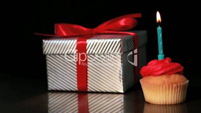 Candle on cupcake blown beside gift