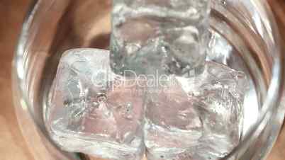 Tongs placing ice into tumbler and whiskey being poured over