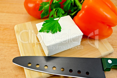 Feta cheese on a board with a knife and vegetables