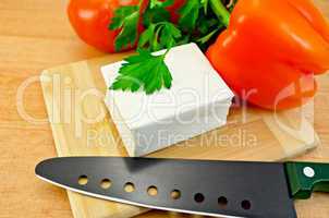 Feta cheese on a board with a knife and vegetables