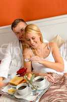 Happy lovers lying bed eating romantic breakfast