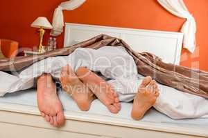 Napping couple barefoot lying under covers bed