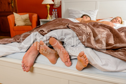 Lovers foot poking out bed covers sleeping