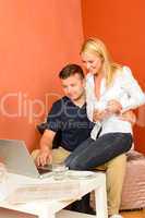 Happy couple sitting looking laptop man holding