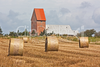 Strohballen auf Getreidefeld auf Sylt. Im Hintergrund die Kirche von Keitum.