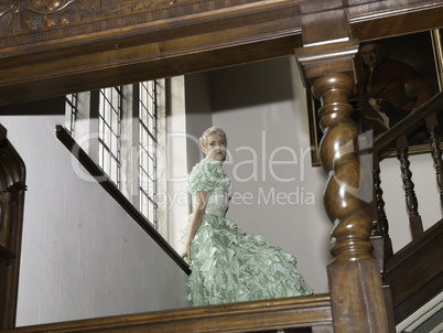 Pretty blond woman standing on stairs with green ball gown