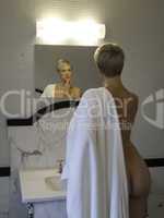 Woman with the towel looking in the bathroom mirrow.