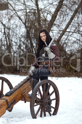 Woman in the medieval costume with a sword sitting on a cannon