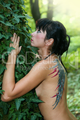 Young woman with painted wings on her back in the forest
