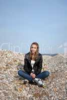 Teenage girl with rollerblades sitting on pebbles