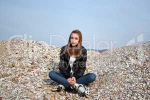 Teenage girl with rollerblades sitting on pebbles