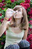 Teenage girl drinking water from the bottle in the flower garden