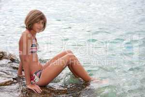 Teenage girl in bikini sitting on a rock in the sea