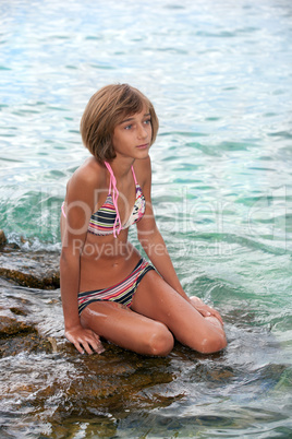 Teenage girl sitting on a rock in the sea