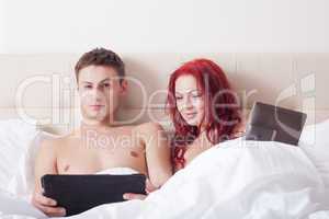 Attractive couple in bed with tablet computers