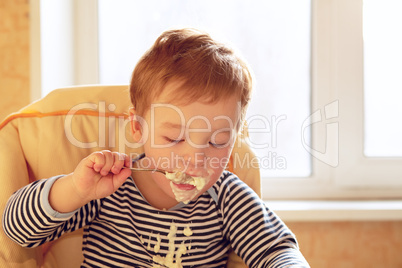 Two year old boy eats porridge in the morning.