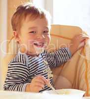 Two year old boy smiles and eating porridge.