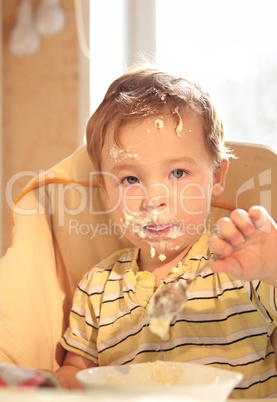 Two year old boy eats porridge in the morning.