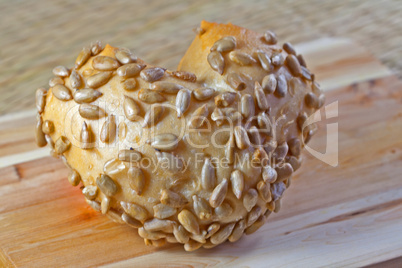 Brötchen in Herzform mit Körnern auf Holzbrett