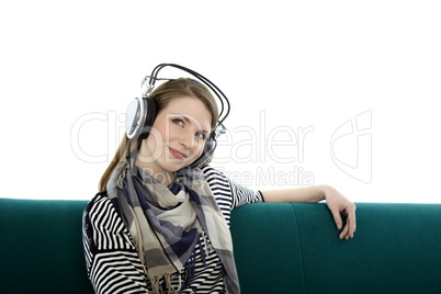 beautiful young smiling woman sitting on a sofa and listens to music with headphones on her head