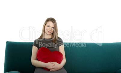beautyful young woman smiling and sitting on a sofa with heart shaped pillow in her hand