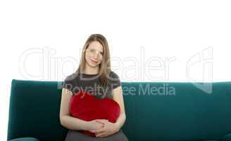 beautyful young woman smiling and sitting on a sofa with heart shaped pillow in her hand