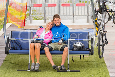 Cuddling couple sitting chair lift with bicycles