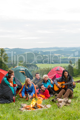 Camping friends playing guitar beside fire nature