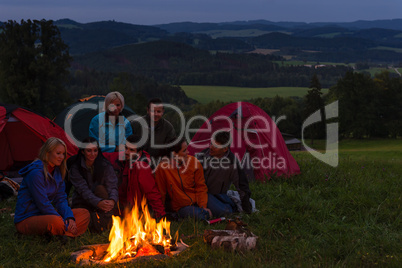 Camping people watching campfire together beside tents
