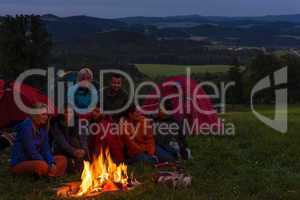 Camping people watching campfire together beside tents