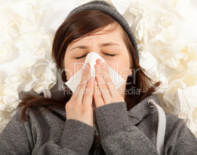 Das junge Mädchen liegt krank im Bett und putzt sich die Nase