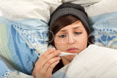 Das junge Mädchen liegt krank im Bett und misst Fieber