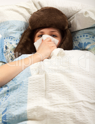 Das junge Mädchen liegt krank im Bett und putzt sich die Nase