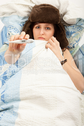 Das junge Mädchen liegt krank im Bett und misst Fieber