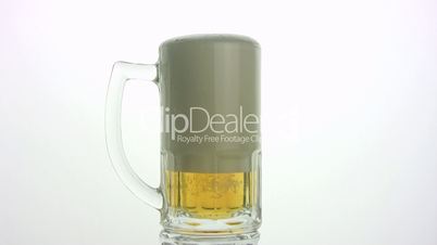 The beer foam is poured through edge of mug. White background