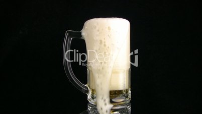 The beer foam is poured through edge of mug. Black background