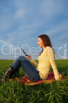 Teen girl reading electronic book outdoors