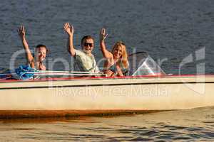 Young people waving from motorboat