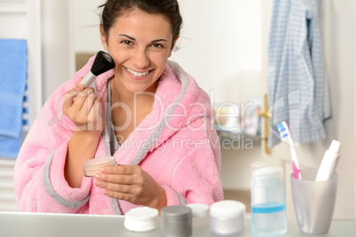 Young woman applying face powder with brush
