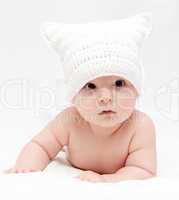 baby in white hat lies on bed