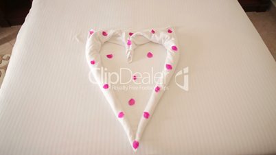 Heart of towels with rose petals on the bed