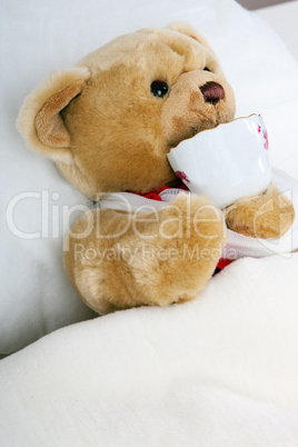 Teddy bear lying in bed and drink cup