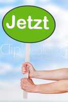 Hands holding a sign with the word jetzt